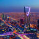 Riyadh skyline at night showing illuminated Kingdom Centre tower and city buildings with traffic on streets below